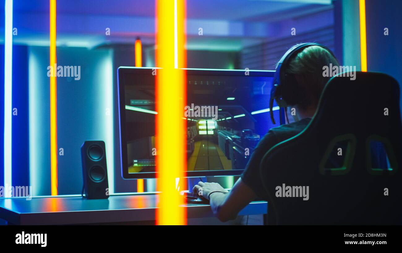 Pro Gamer spielt in der First Person Shooter auf seinem Personal Computer. Spricht mit Teamkollegen über Kopfhörer. Neonfarbenes Zimmer. Online-eSport Stockfoto