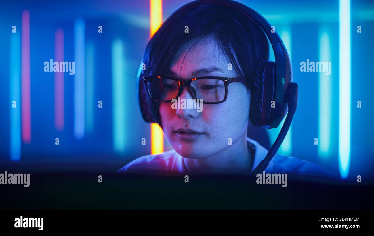 Professionelle Ostasiatische Gamer spielen in Online-Video-Spiel auf seinem Computer. Gespräche mit seinem Team über Mikrofon. Zimmer mit Neonlicht Stockfoto