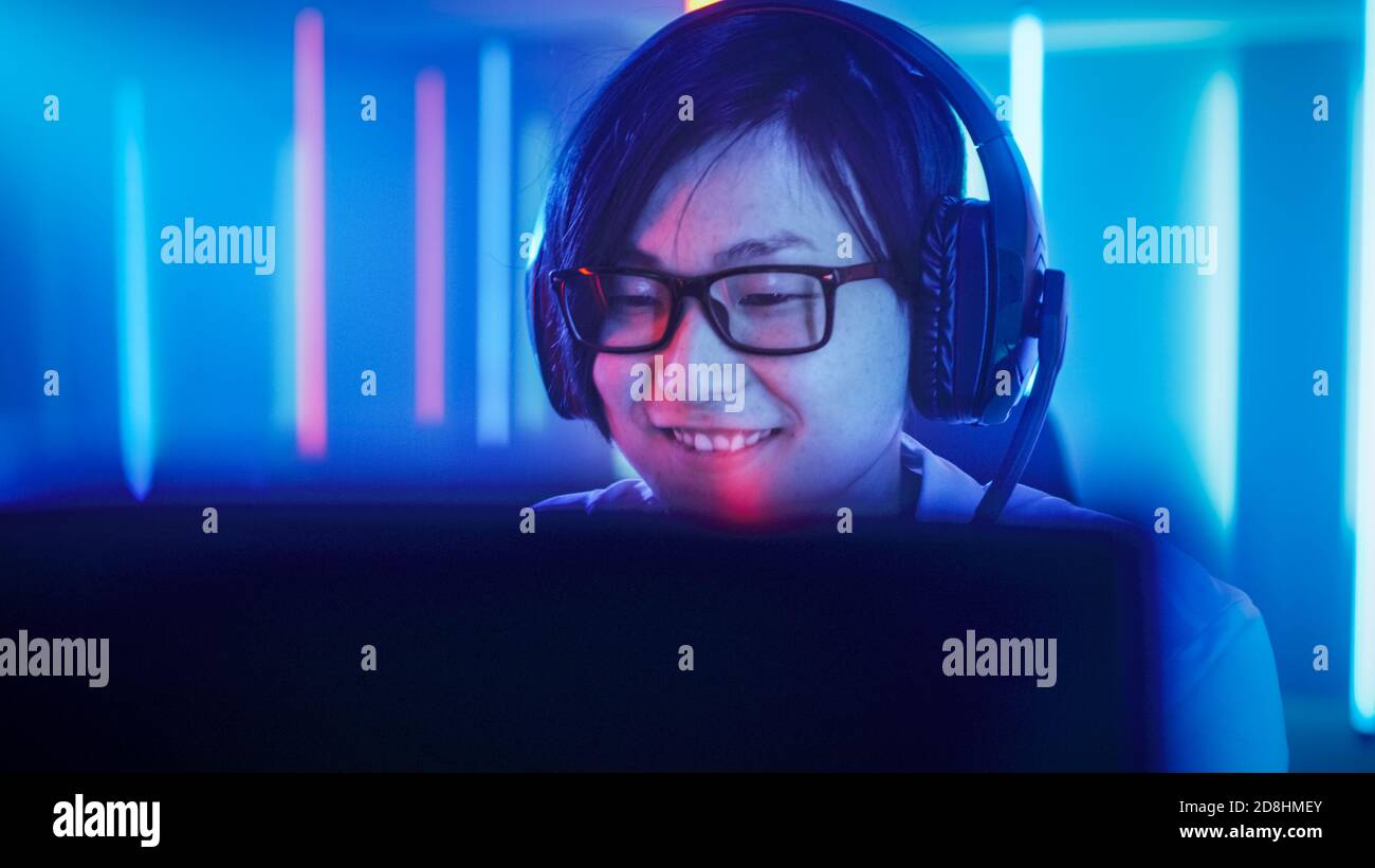 Professionelle Ostasiatische Gamer spielen in Online-Video-Spiel auf seinem Computer. Er lächelt. Zimmer mit Neonlicht im Retro Arcade-Stil Stockfoto