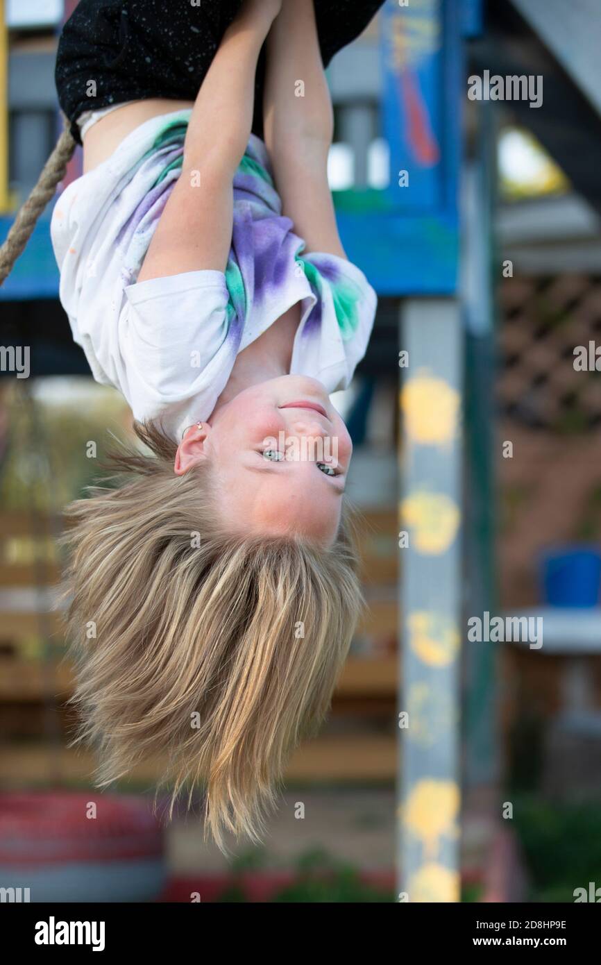 Schönes kleines Mädchen hängt kopfüber auf dem Spielplatz. Kleines Mädchen lächelt in die Kamera. Stockfoto