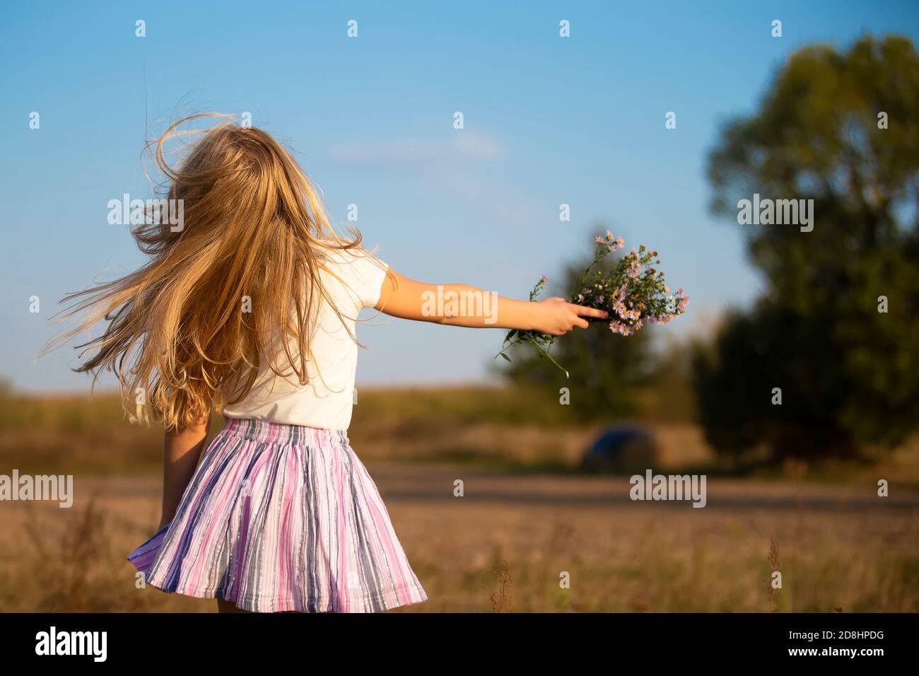 Glückliches kleines Mädchen läuft auf der Wiese mit einem Blumenstrauß. Kind auf einem schönen Sommerfeld gegen den blauen Himmel. Stockfoto