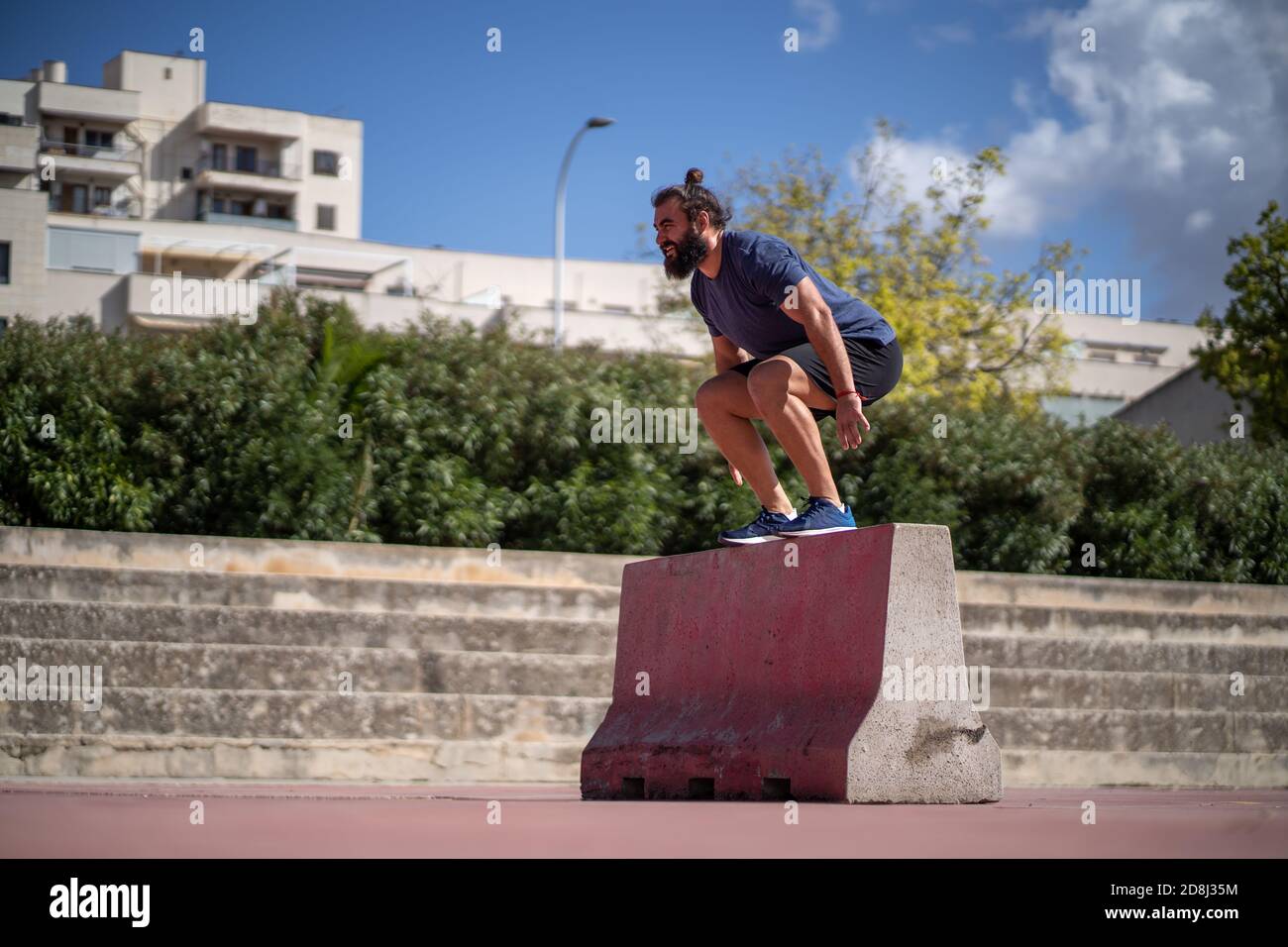 Mann trainiert mit Kniebeugen springt auf einer Plattform in der Mitten in einem Hof Stockfoto