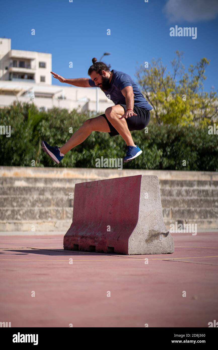 Mann trainiert hohe Leistung springt über ein Hindernis in der Mitten in einem Hof Stockfoto
