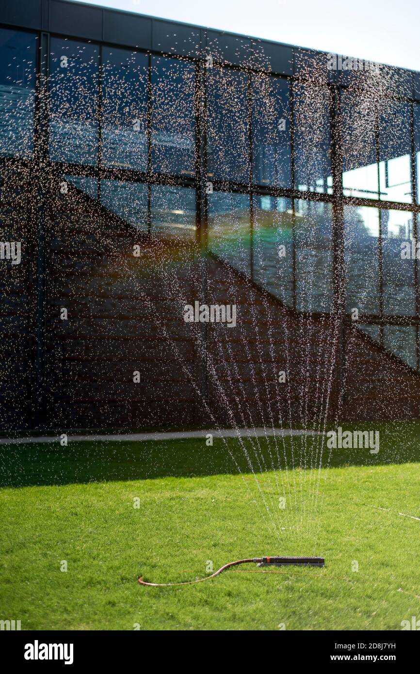 Wasserregner auf dem Rasen vor einem öffentlichen Gebäude mit Regenbogen Stockfoto