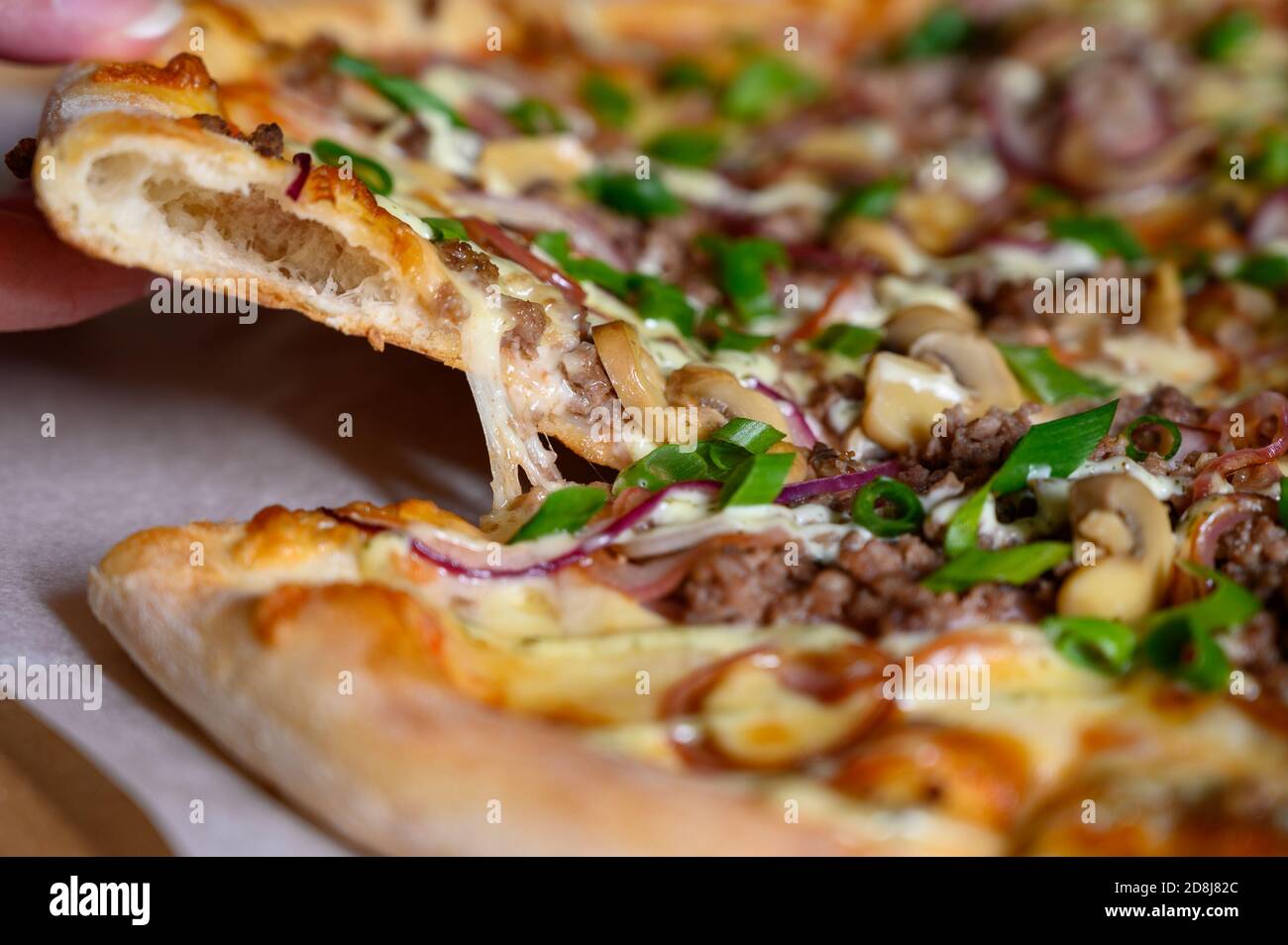 Nahaufnahme einer Hand bricht ein Stück Pizza ab. Pizza mit Pilzen, Zwiebeln und Käse. Stockfoto