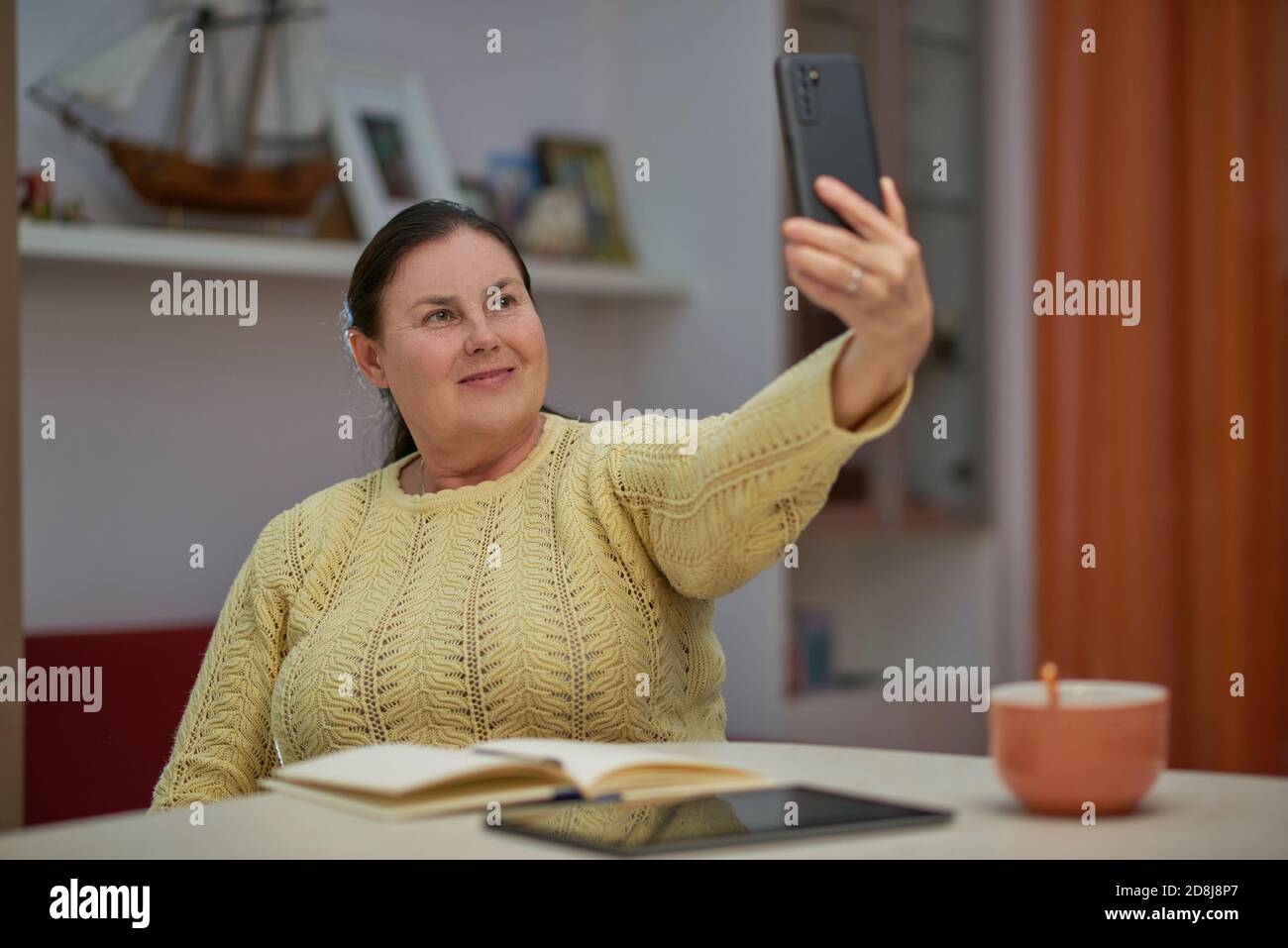 Ältere Frau in gelben Pullover nimmt Selfie mit Smartphone Stockfoto Ältere Frau in gelben Pullover nimmt Selfie mit Smartphone Stockfoto