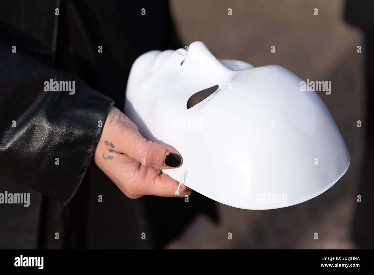 Die weibliche Hand im Vordergrund mit einem kleinen Tattoo hält die weiße Theatermaske. Stockfoto