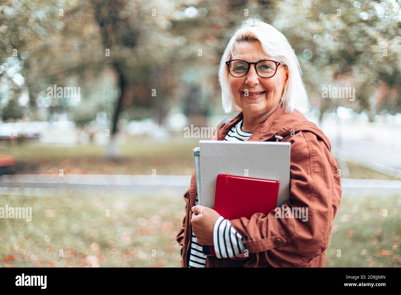 Erwachsene kaukasische blonde Lehrerin Frau in Brille für die Sicht mit Büchern, Notizbuch und Zeitschriften Blick auf die Kamera im Park Stockfoto
