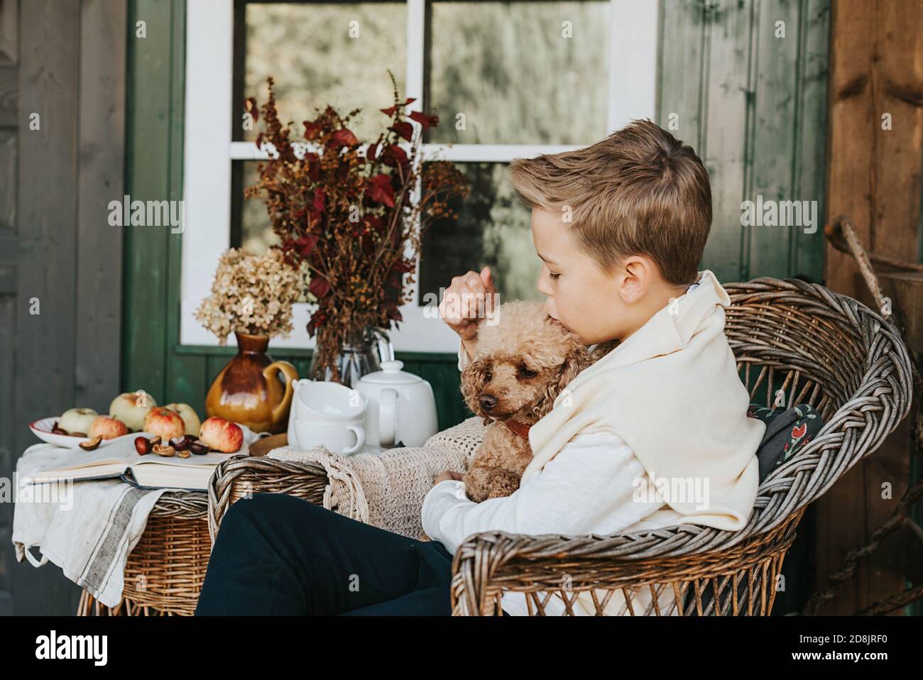 Ein Junge mit seinem Hund im Sessel, der sich ausruhte Die Veranda auf dem Hinterhof mit Herbstdekorationen Stockfoto