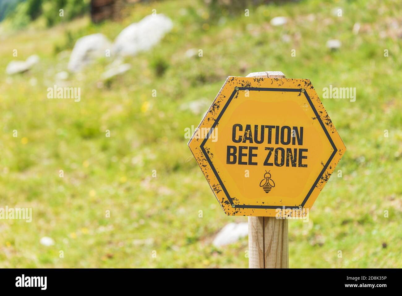 Bee Zone Warnung knallig gelb und schwarz Warnschild auf einem Holzpfosten vor einem Bergweg Hintergrund gesetzt. Stockfoto