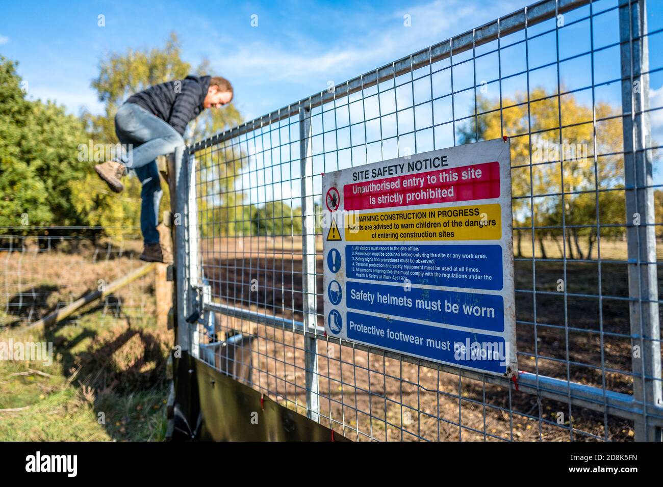 Erwachsener Mann klettert Zaun in eine kontaminierte Heide, die für militärische Ausbildung verwendet wird. Stockfoto