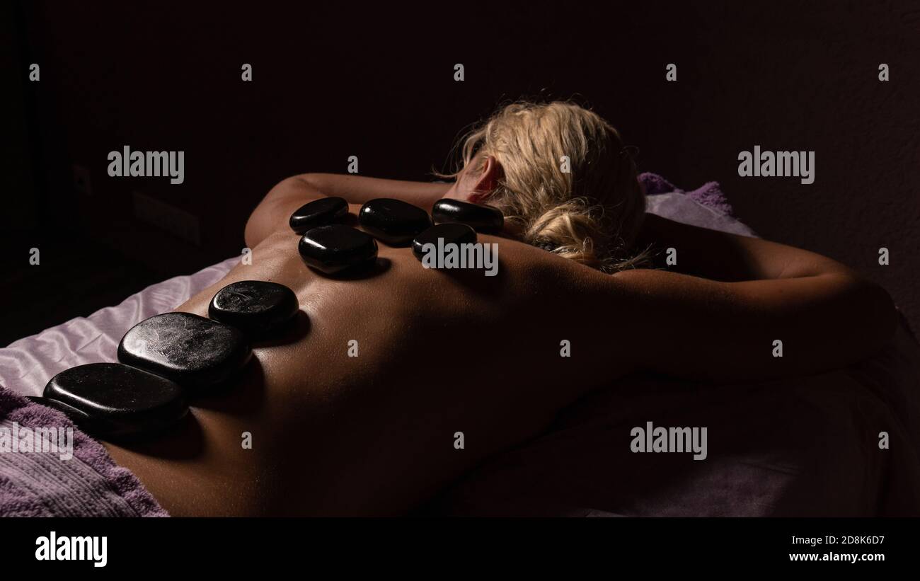 Thai Massage mit Steinen auf schwarzem Hintergrund , liegt ein Mädchen in der dunklen, blonden Stockfoto