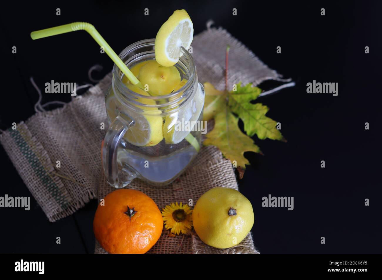 Gesunde Limonade in einem Glas mit Zitronenscheiben und einem Trinkschlauch auf einem dekorierten schwarzen Schreibtisch aus Holz. Nahaufnahme, selektiver Fokus Stockfoto