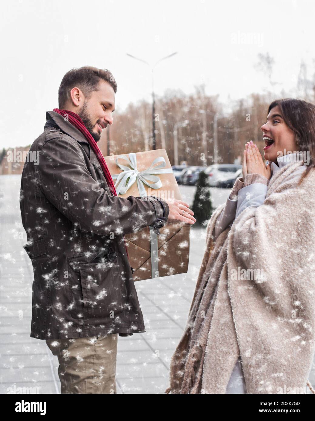 Mann, der seiner Freundin ein Weihnachtsgeschenk gibt. Emotional überrascht glückliches Mädchen erhält ein Geschenk draußen in schneebedeckten Wetter. Stockfoto