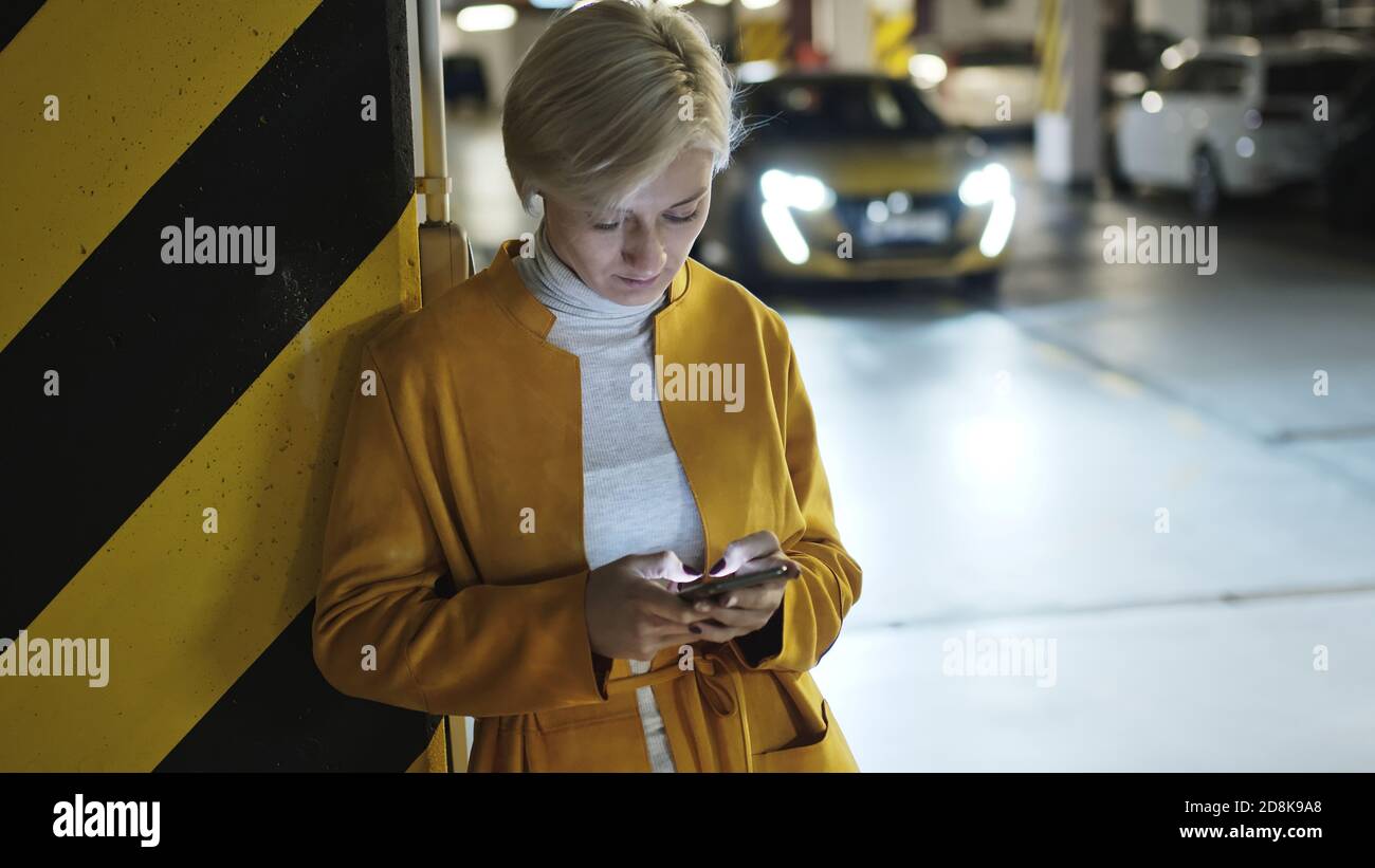Junge modische blonde kaukasische Frau mit Smartphone in der Tiefgarage. Hochwertige Fotos Stockfoto
