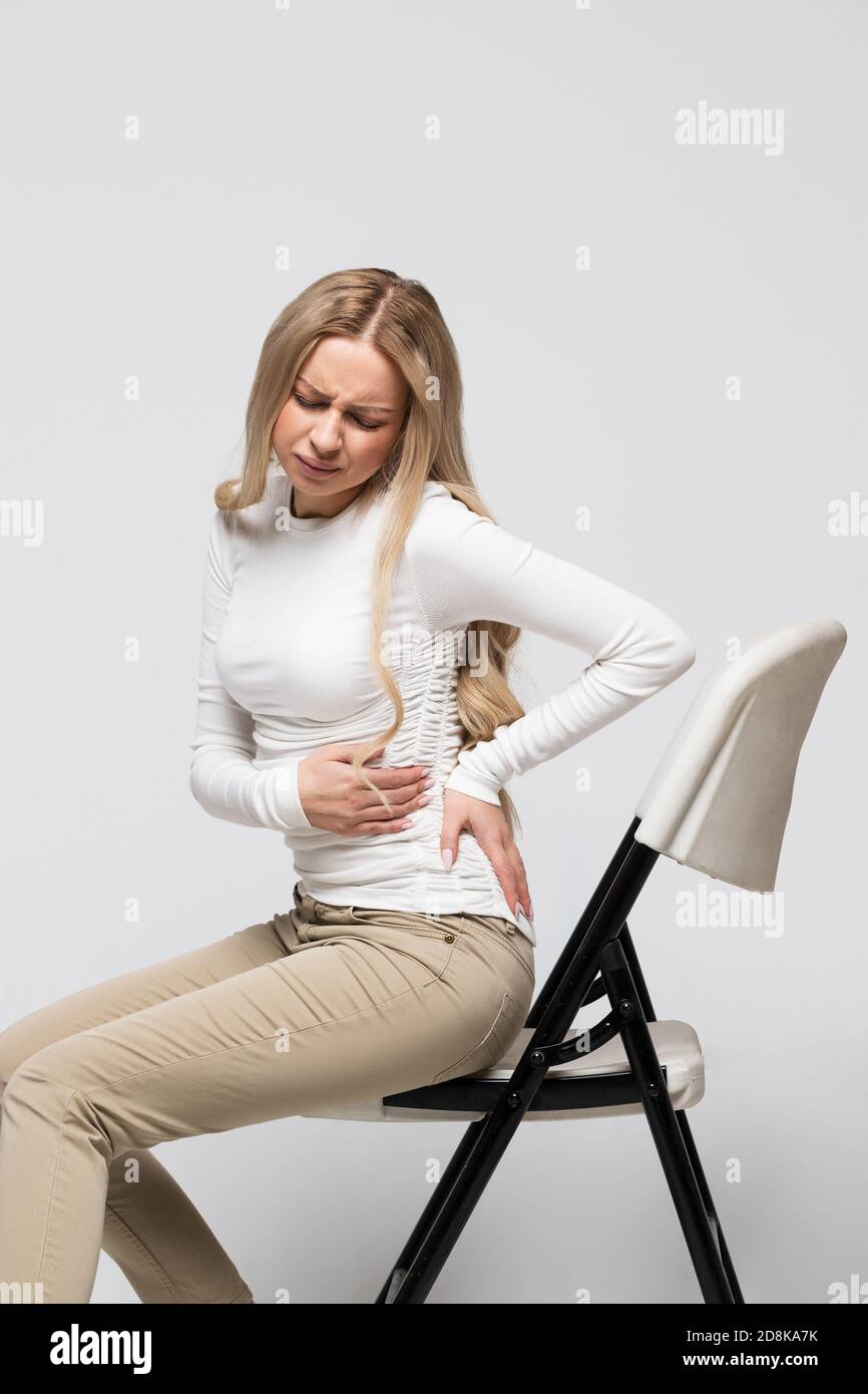 Frau mit Schmerzen, Muskel- oder chronischen Nervenschmerzen im Rücken, sitzend auf einem Stuhl. Erkrankungen des Bewegungsapparates, der Wirbelsäule, Skoliose, Osteoporose Stockfoto