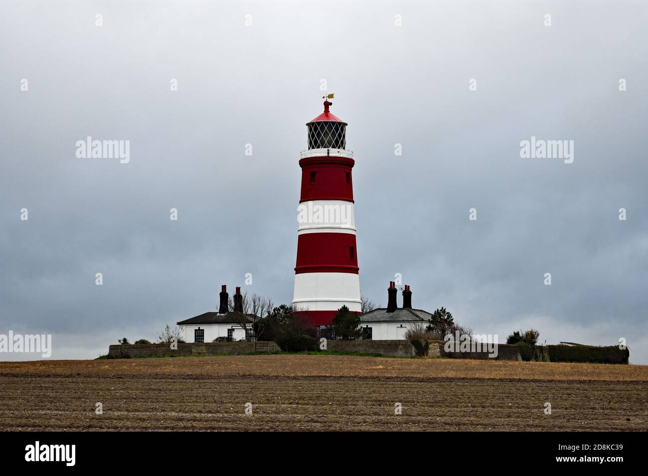 Der rot-weiß gestreifte Happisburgh Leuchtturm an der Norfolk Küste, England. Der Leuchtturm steht an einem bewölkten Tag in einem schlammigen Feld. Stockfoto