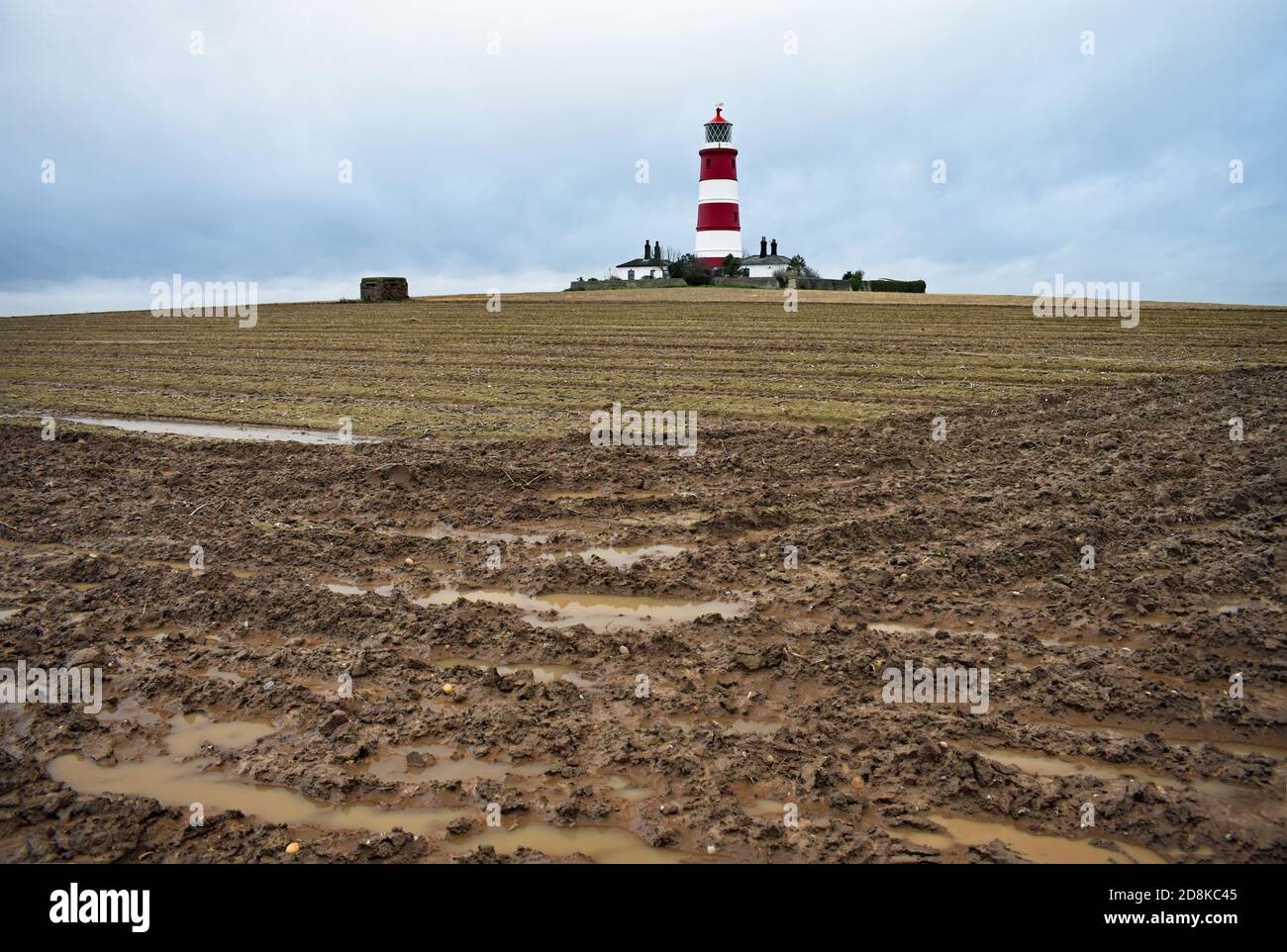 Der rot-weiß gestreifte Happisburgh Lighthouse entlang der Norfolk Küste, England.der Leuchtturm steht hoch in einem schlammigen Feld mit einem Pillbox. Stockfoto