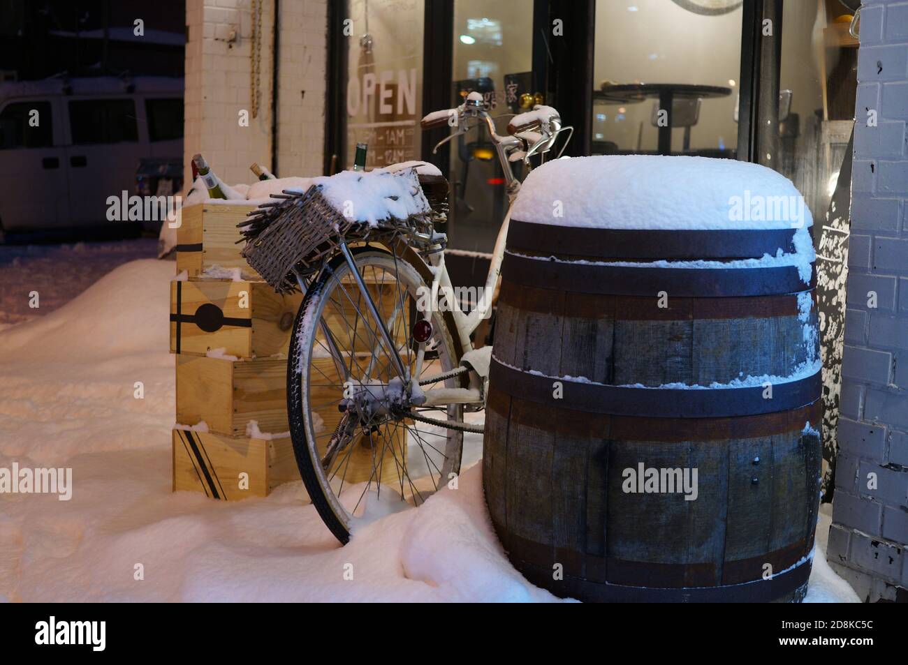 Holzweinfass, Weinsärge und Fahrrad mit frischem weißen Schnee in der Nähe der Glas-Café-Tür am Abend bedeckt Stockfoto