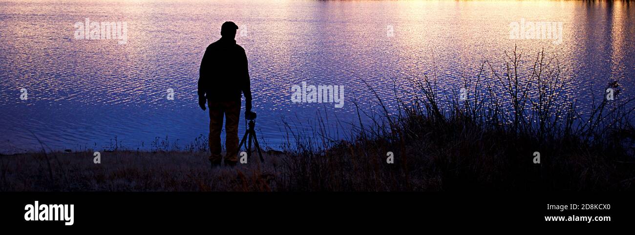 Mann mit dem Rücken zur Kamera und Blick auf das im See reflektierte Licht Stockfoto