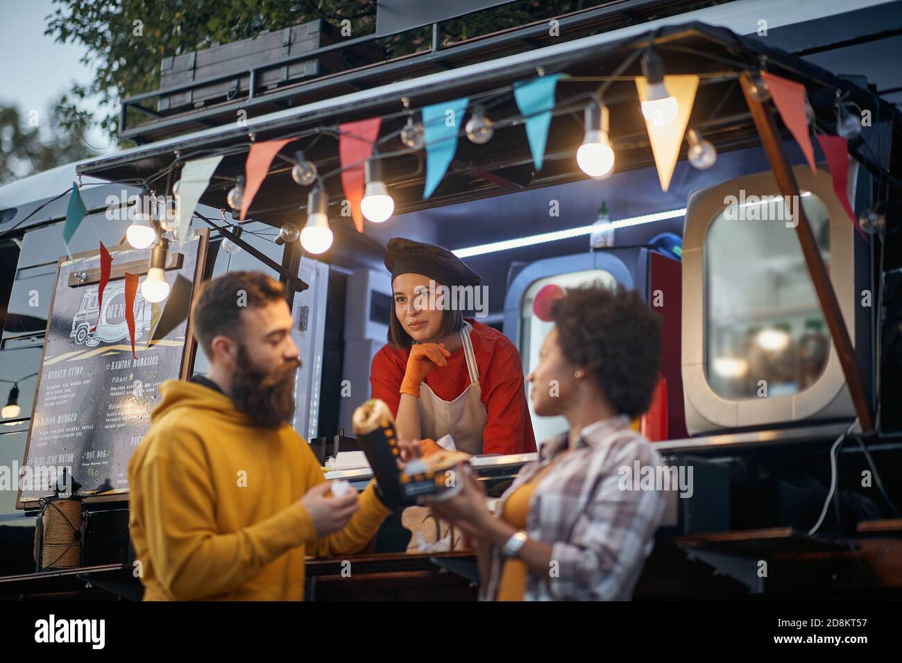 Junge Mitarbeiterin im Fast-Food-Service, die Kunden anschaut, die essen, Reaktion erwartet Stockfoto