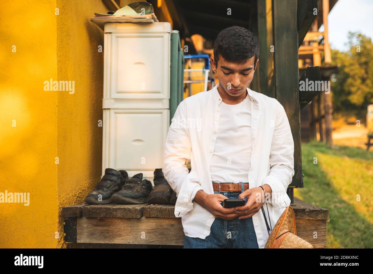 Ein junger Mann, der sich in der Nähe alter Schuhe ausruhen und Smartphone für Messaging verwenden kann. Modekonzept Fotografie Stockfoto