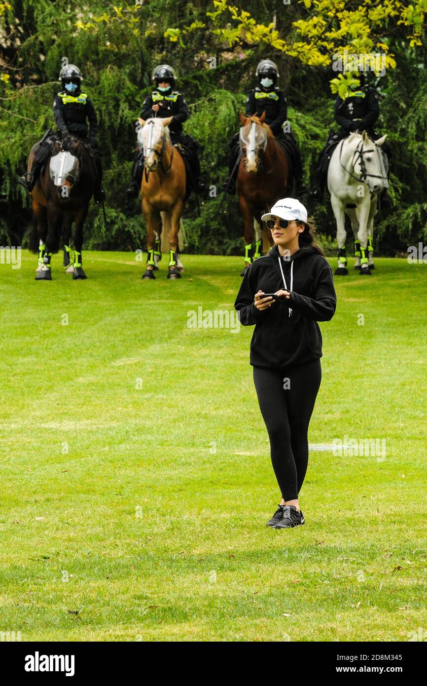 Melbourne, Australien 31 Oct 2020, eine Frau protestiert gegen die Politik der staatlichen Regierung auf COVID-19 und China und beobachtet Lautsprecher, wie sie von vier berittenen Polizeibewegungen beobachtet wird, die im Park als Teil einer Polizeiaktion waren, um eine kleine Anzahl von regierungsfeindlichen Protesten zu stören. Kredit: Michael Currie/Alamy Live Nachrichten Stockfoto