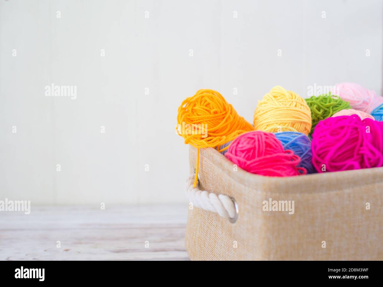 Leuchtend farbige Fäden zum Stricken in einem Korb auf einem Holzhintergrund Stockfoto