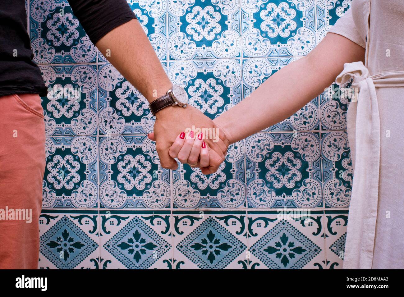 Paar hält die Hände vor einer eingehüllten Wand Blaue Azulejos-Kacheln Stockfoto