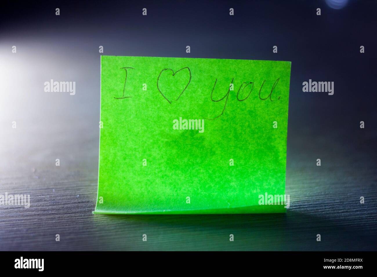 Ich liebe Sie Nachricht auf hellem grünen Blatt Schreibpapier Notiz mit Herz auf blauem Hintergrund geschrieben. Stockfoto