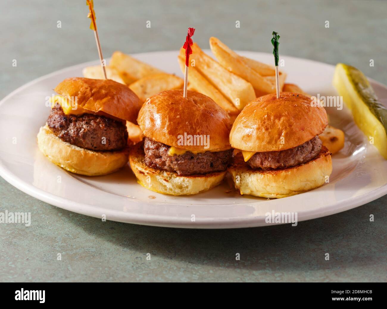 Drei Cheeseburger-Slider mit Pommes Frites und einer Gurke Eine weiße Platte Stockfoto