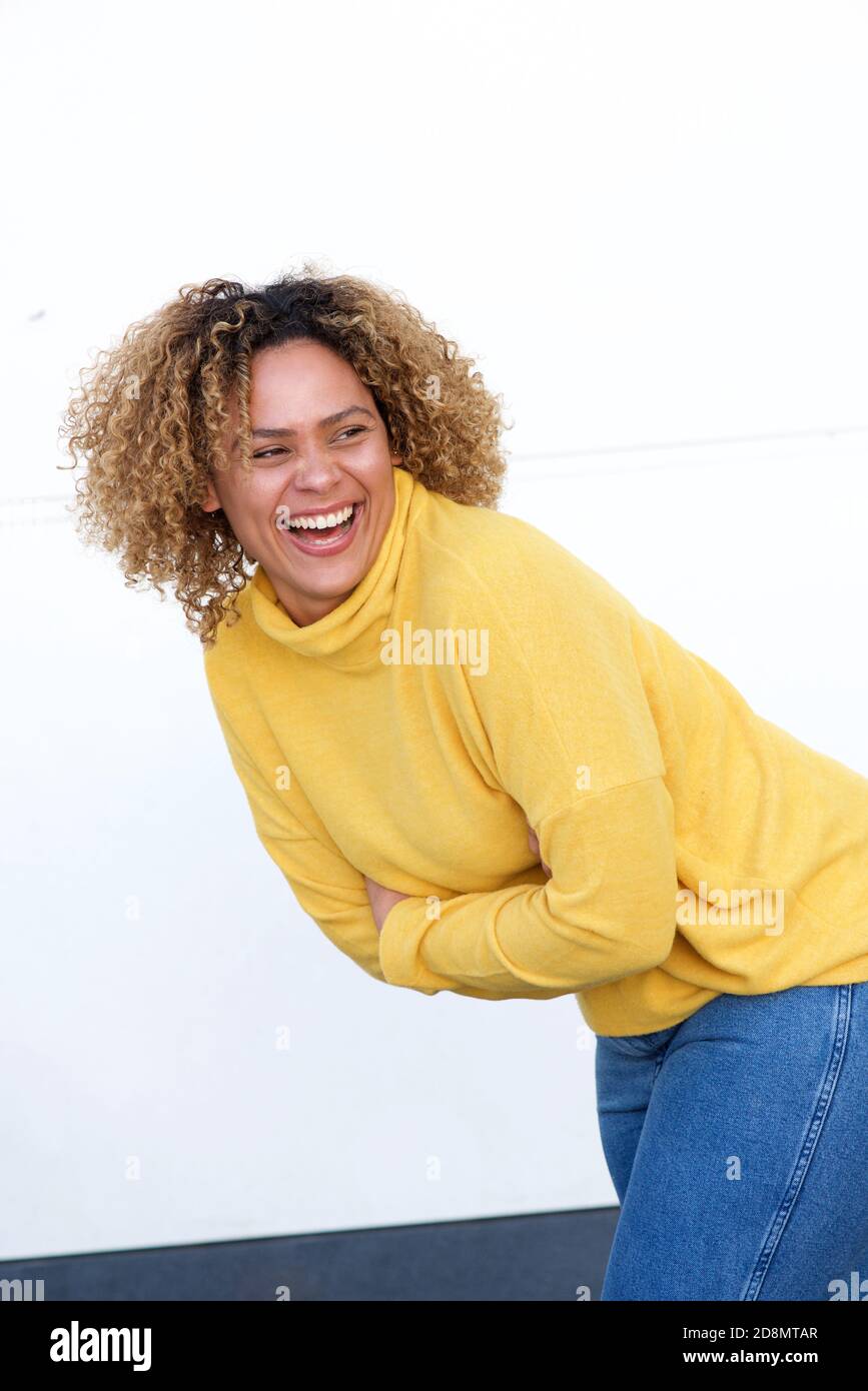 Porträt einer attraktiven jungen afroamerikanischen Frau, die mit Armen lacht Durchzogen von einer weißen Wand Stockfoto