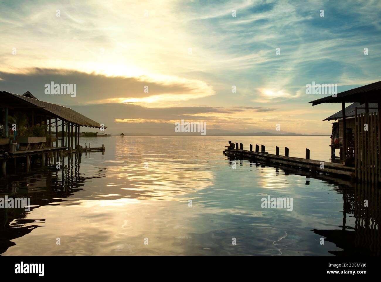 Wasserlandschaft von Stelzenhäusern mit einem Gitarristen am Ende eines Steg. Sonnenuntergang vibes mit Wasserspiegelungen in Bocas del Toro, Bocas Town, Panama. Oktober 2018 Stockfoto