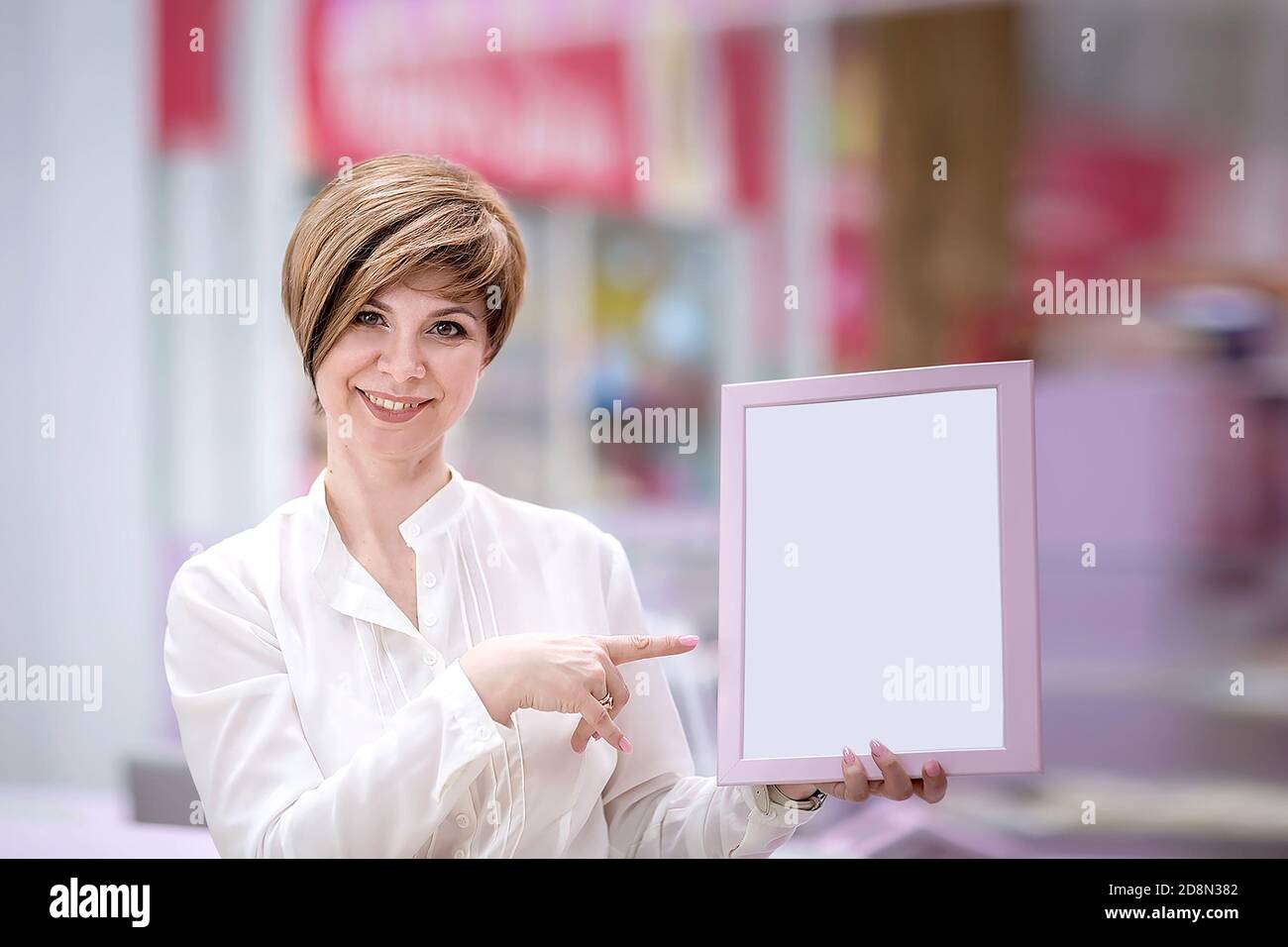 Eine schöne junge Frau steht in einem Einkaufszentrum (oder Restaurant), hält einen Rahmen für Anzeigen. Speicherplatz kopieren. Leerzeichen für Text. Das Konzept der Kleinunternehmer Stockfoto