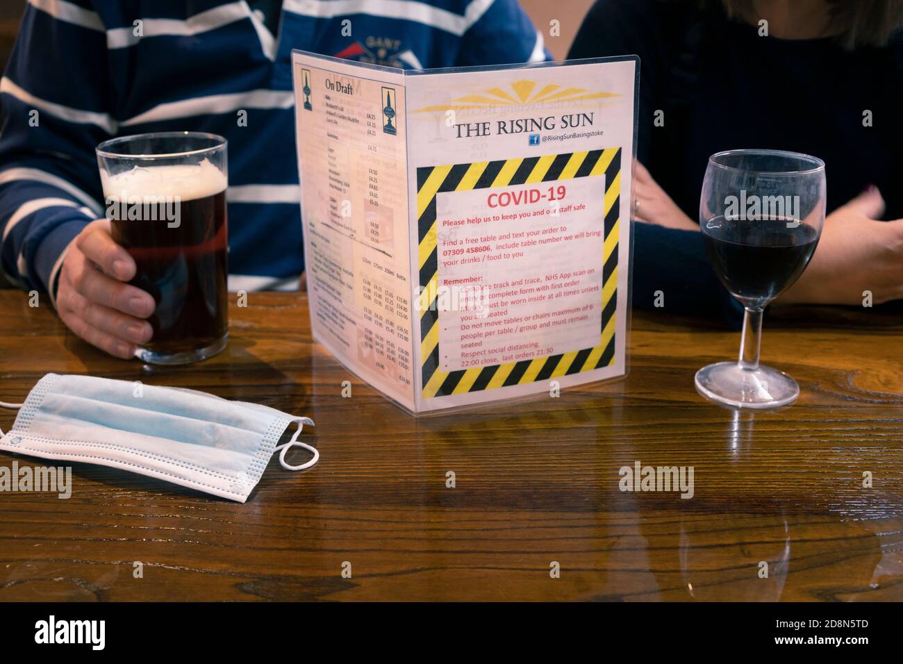 Ein Mann und eine Frau trinken in einem Pub mit Covid-19 Coronavirus Regeln und Einschränkungen auf dem Tisch und eine Einweg-Gesichtsmaske. Basingstoke, Großbritannien Stockfoto