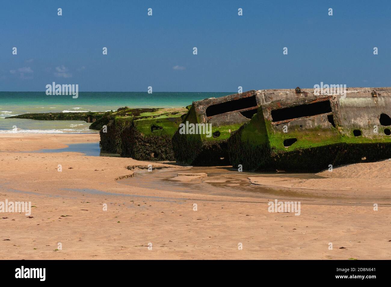 Bei Ebbe in Arromanches, Calvados, Normandie, Frankreich, Die Menschen können zu Fuß an den Rand des Wassers auf dem Zweiten Weltkrieg ‘Gold Beach’ zu erreichen - aber nicht betreten - vorgegossene Betonabschnitte von Port Winston oder Mulberry Harbour B. Dies war der 600,000-Tonnen-vorgefertigte tragbare Hafen, der über den Ärmelkanal geschleppt wurde, Vor der Küste montiert und dann für 10 Monate nach der Operation Overlord ‘D-Day’ Invasion vom 6. Juni 1944 verwendet, um 2.5 Millionen britische und kanadische Truppen, eine halbe Million Fahrzeuge und vier Millionen Tonnen Vorräte zu landen. Stockfoto