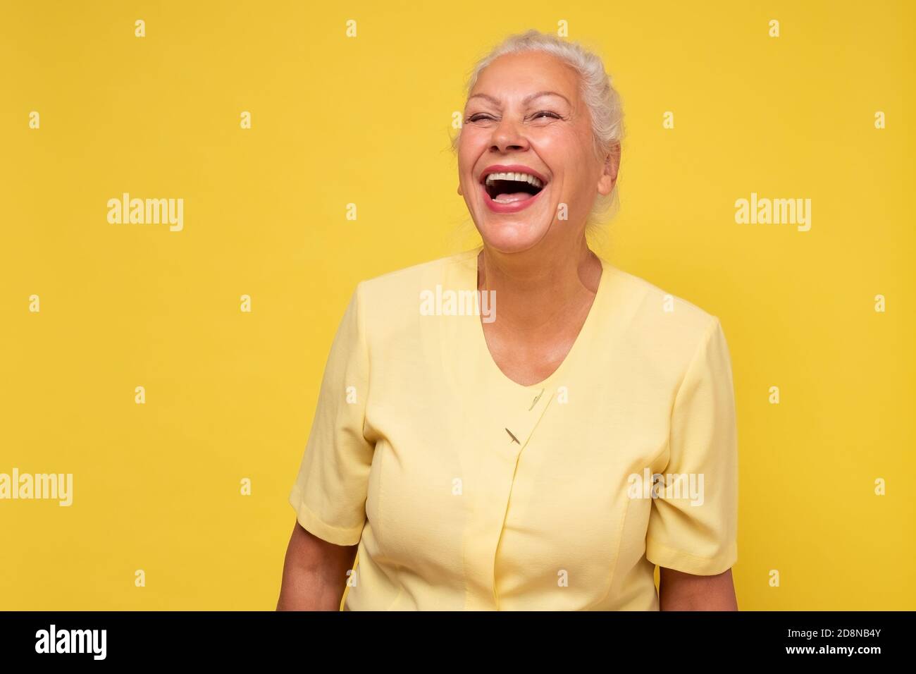 Ältere Frau lächelt glücklich lachend an der Kamera an der gelben Wand. Stockfoto