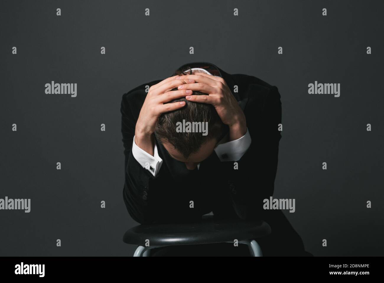 Studioportrait eines jungen kaukasischen Mannes im Smoking, Hände im Haar, traurig nach unten schauend, vor schlichtem Studiohintergrund Stockfoto