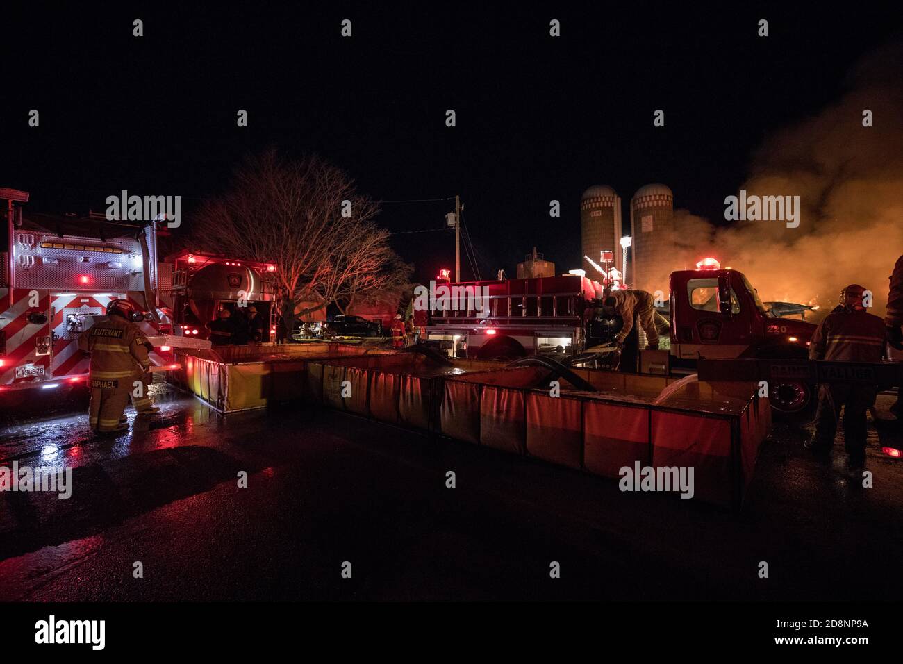 Lodernde Feuerscheune. Feuerwehrauto mit Tankwagen und Pool. Stockfoto