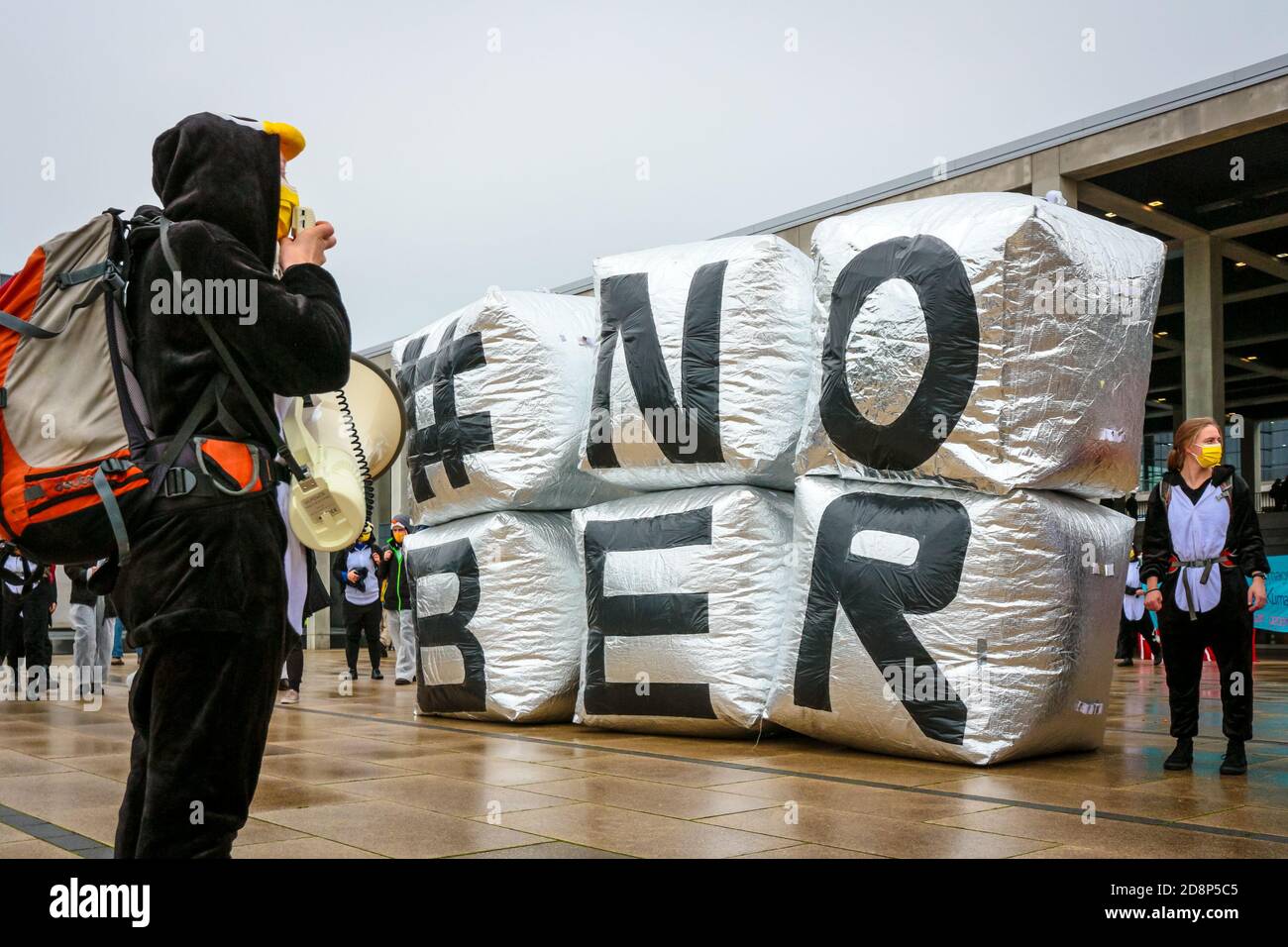 Protestor im Pinguin-Kostüm mit Megaphon am '#NOBER'-Schild als Klimaaktivist protestieren gegen die Eröffnung des Flughafens Berlin Brandenburg (ber). Stockfoto