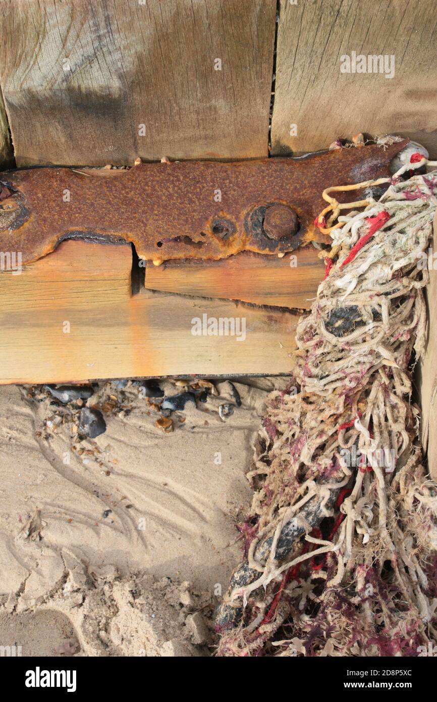 Nahaufnahme Meereswand Küstenbarriere in Holz zusammengeschraubt Metallbolzen Nüsse braun Rost Farbe im Salzwasser weißen Sand, Baumwolle Fischernetz Algen Stockfoto