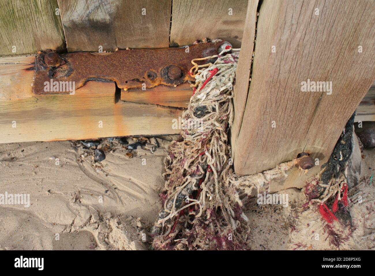 Nahaufnahme Meereswand Küstenbarriere in Holz zusammengeschraubt Metallbolzen Nüsse braun Rost Farbe im Salzwasser weißen Sand, Baumwolle Fischernetz Algen Stockfoto