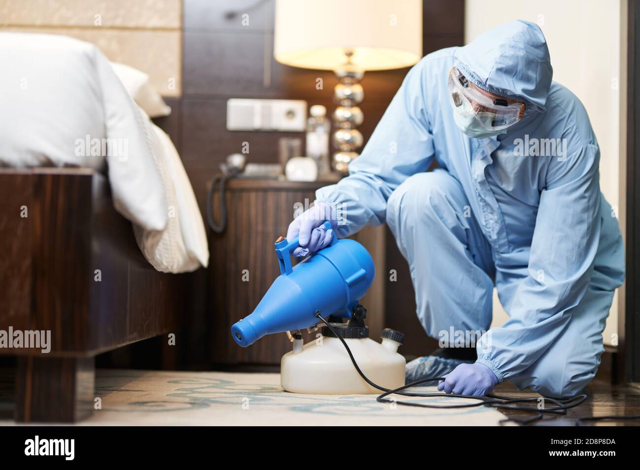 Mann in Biogefährdungsanzug und Handschuhe, die das Schlafzimmer im Hotel desinfizieren. Coronavirus und Quarantänekonzept Stockfoto