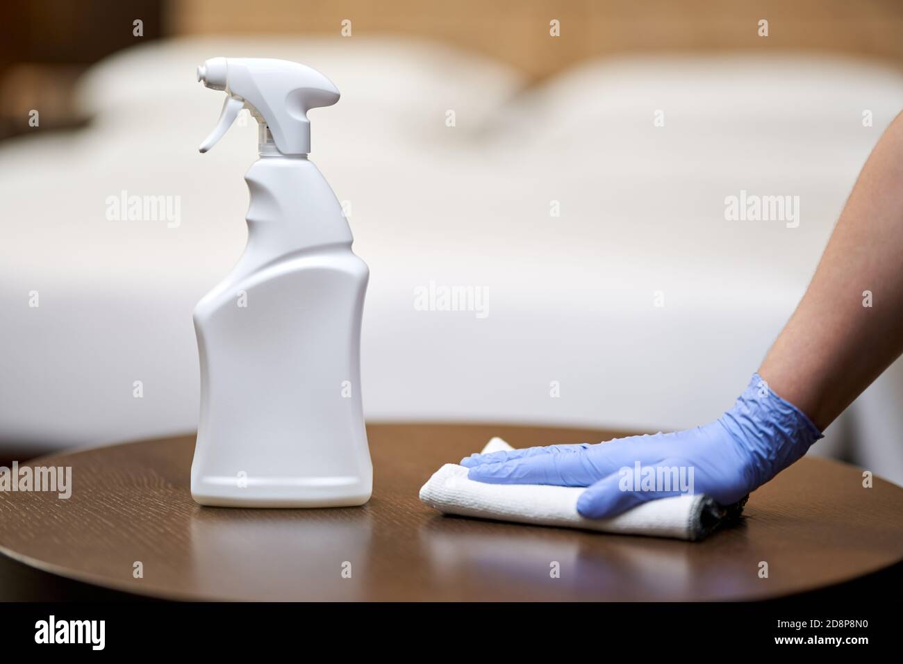 Nahaufnahme des Zimmermädchens, das den Holztisch mit einem Sprühwaschmittel im Hotelzimmer putzte und polierte. Housekeeping- und Hygienekonzept Stockfoto