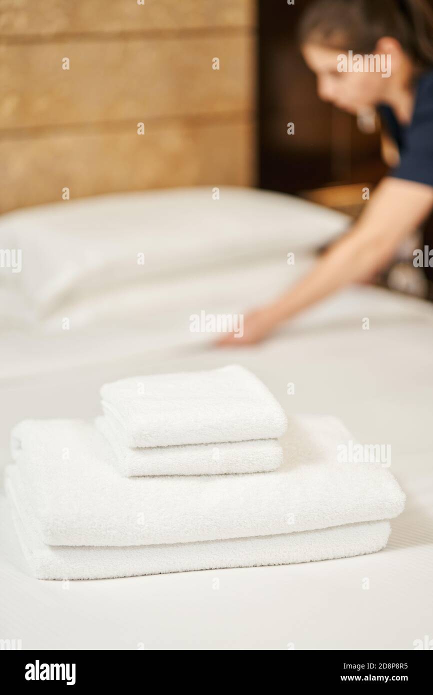 Saubere Handtücher liegen im Bett mit Zimmermädchen im Hintergrund. Servicekonzept des Hotels Stockfoto