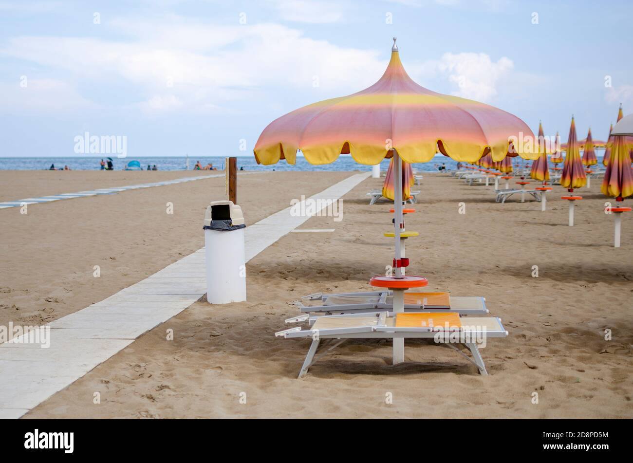 Italienischer Strand mit Sand und Sonnenschirmen und Menschen in der Entfernung Stockfoto