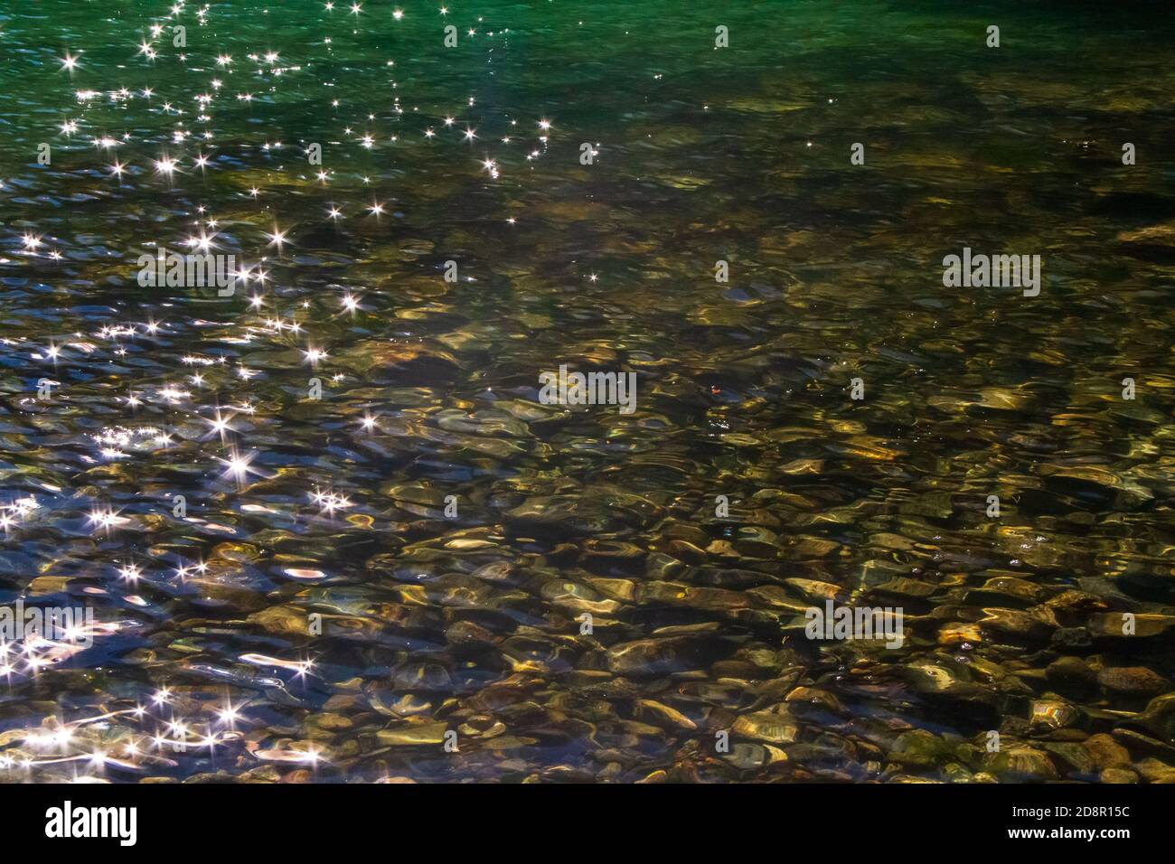 Reflektiertes Sonnenlicht auf dem Wasser, mit Felsen und Austern unter der Oberfläche. Stockfoto