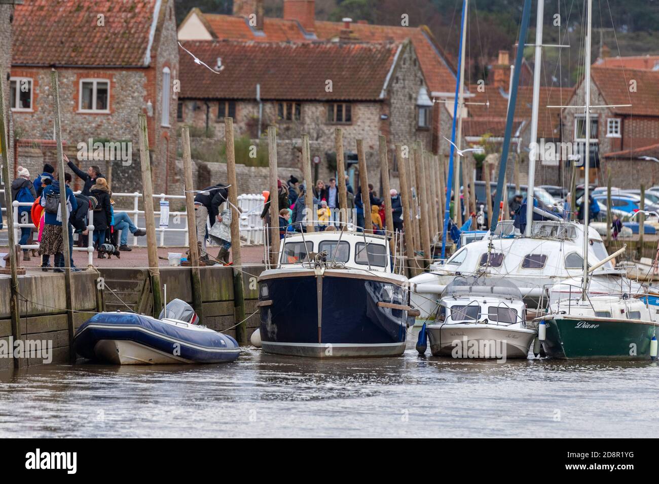 Boote entlang der Mauer bei blakeney an der Nordküste norfolks mit Touristen, die mit Linien entlang der Uferstraße krabben. Stockfoto