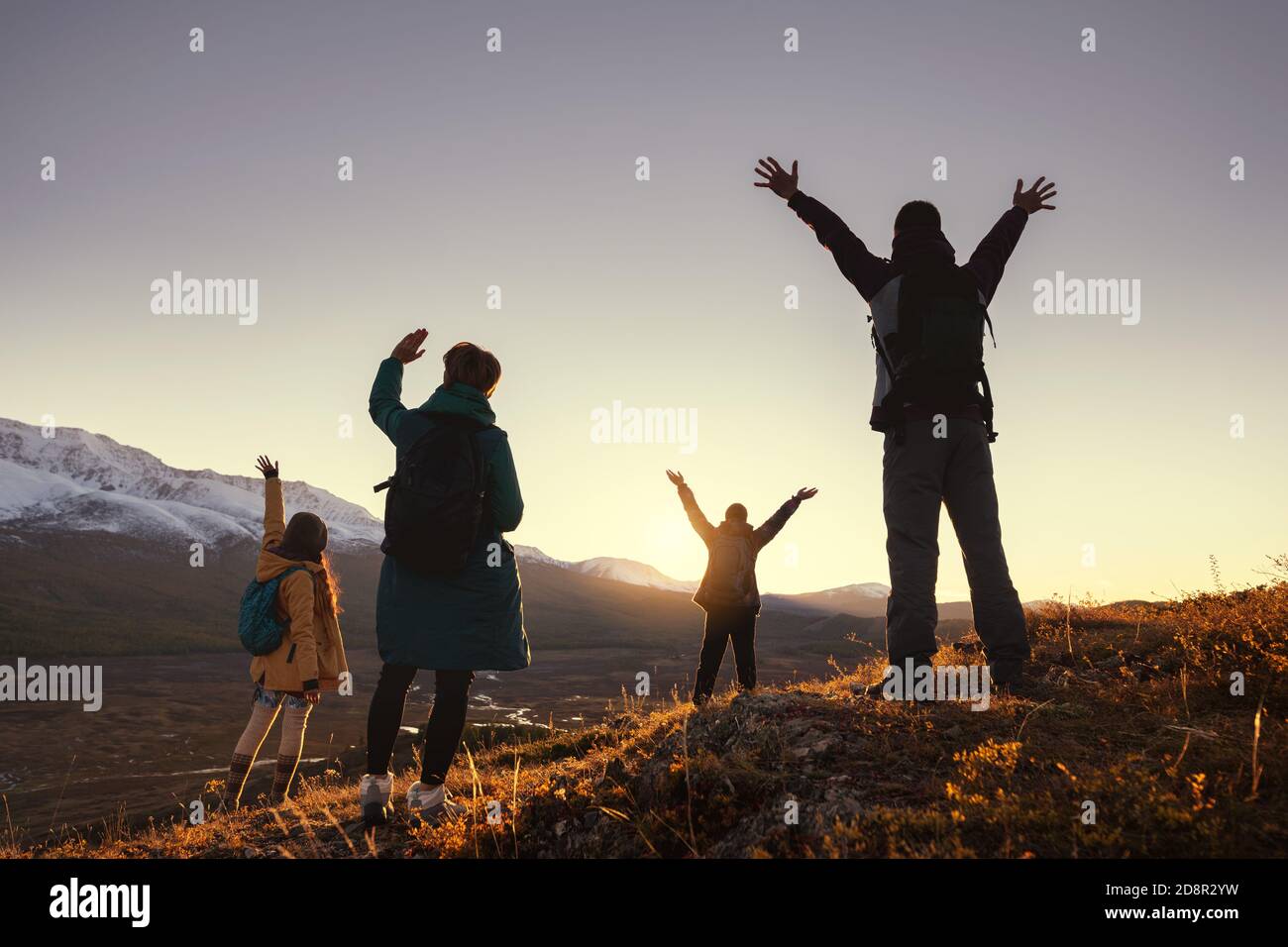 Vier junge Wanderer grüßen mit erhobenen Armen Sonnenuntergang in den Bergen Stockfoto