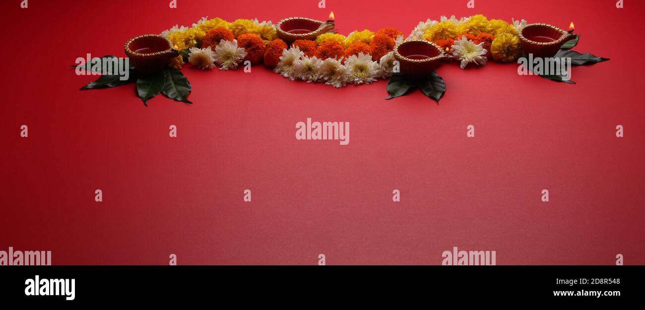 Blume Rangoli für Diwali oder Pongal Festival gemacht mit Marigold oder Zendu Blumen und Clay Öllampe über rotem Hintergrund. Kopierraum. Licht auf der linken Seite Stockfoto